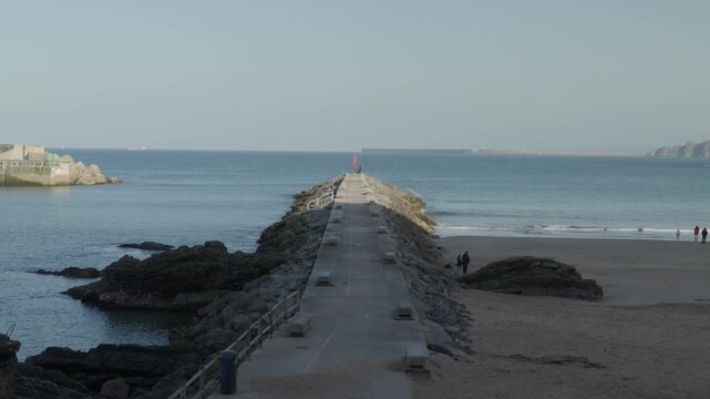 Long stone jetty stretching into the Atlantic Ocean in Cand&aacute;s, Asturias, Spain. Scenic coastal view with calm sea, rocky shoreline, and a distant horizon creating a peaceful maritime landscape.