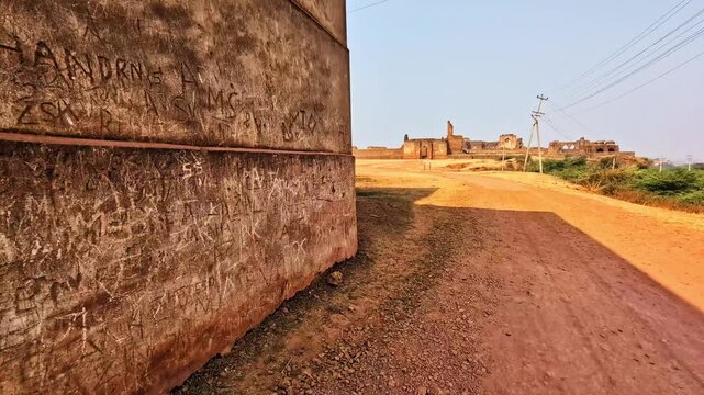 graffiti scratched on fort walls with mud pathway, current pole, trees and sky at bidar, karnataka, india. day time, pov shot, hand held shot, 4k.