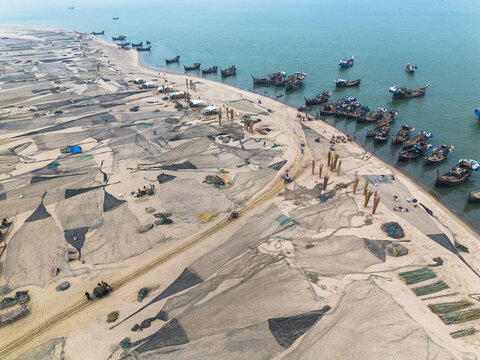 Aerial view of fishing nets spread across the sandy expanse where the beach meets the tranquil sea at Cox's Bazar, Chittagong Division, Bangladesh.