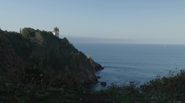 Lighthouse standing on a dramatic coastal cliff overlooking the Cantabrian Sea in Cand&aacute;s, Asturias, Spain. Scenic Atlantic coastline with rugged cliffs, calm ocean waters and clear sky in Spain