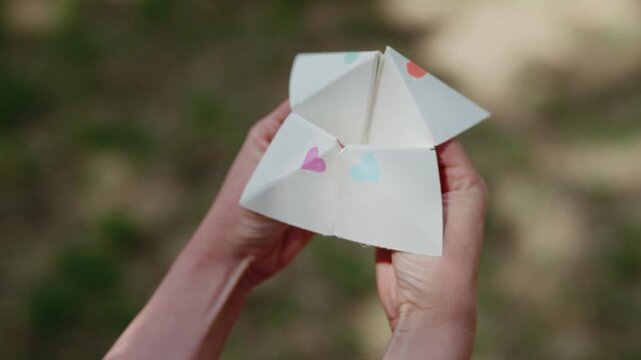 a young woman playing with and operating paper fortune teller aka chatterbox in lush garden