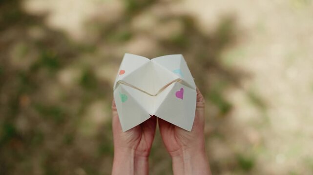 a young woman playing with a paper fortune teller aka chatterbox in lush garden, revealing 'outcomes'