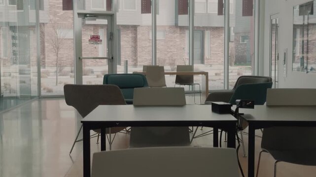 Slow upward reveal of empty classroom tables and chairs by glass windows