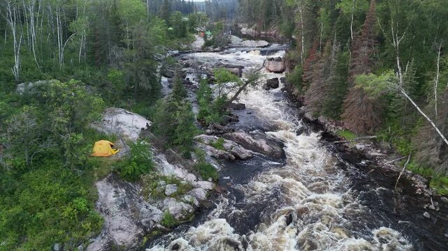 Turtle Falls on the Manigotagan River in Manitoba water flowing over exposed Canadian Shield granite rocks. Summer boreal forest surrounds the falls and campers with tents.