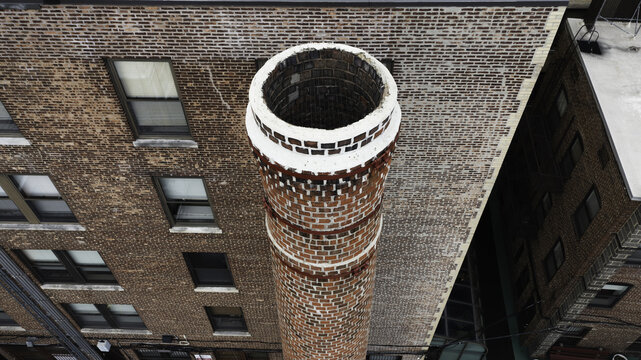 Aerial view of a towering red brick chimney, adorned with white bands, piercing the sky amidst the urban landscape, Summit, New Jersey, United States.