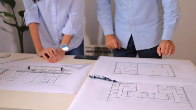 Two architects discussing blueprints and plans for a new building project, collaborating in their office and using professional drawing tools to make precise measurements