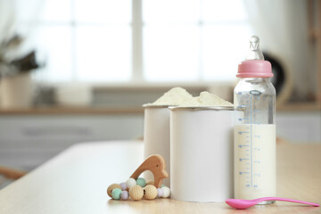 Jars of powdered baby milk formula with bottle and rattle on table in kitchen