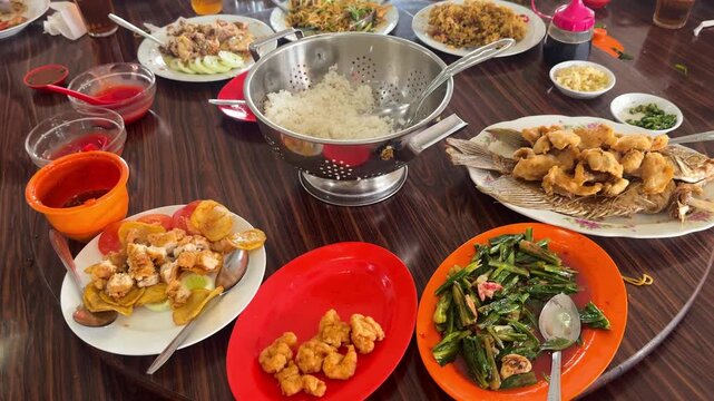Chinese restaurant table scene of rice,chow mein fried noodles,egg foo young,fried fish and shrimp or prawn, Stir-fried Chinese Greens and steamed chicken with fried garlic on a rotating wooden table.