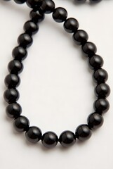 Fototapeta premium Beads made of smooth black stone are arranged in a curved line against a clean white background.