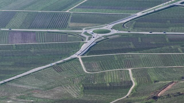 Aerial view of a roundabout where multiple roads converge amid a landscape of patterned fields, creating a geometric tapestry, Mittelwihr, Grand Est, France.