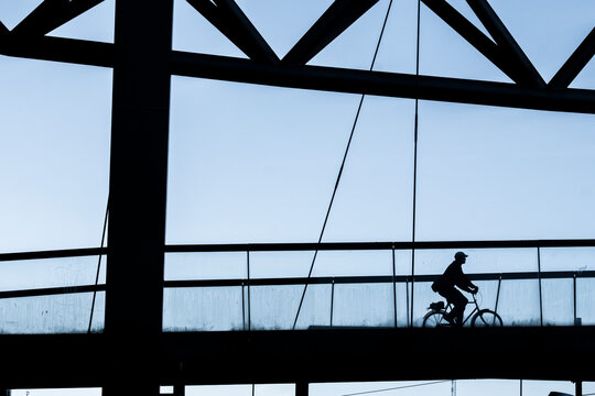 Minimal bridge structure in urban Oslo Norway with cyclist silhouette commuting under sky in daylight during autumn showing graphic motion