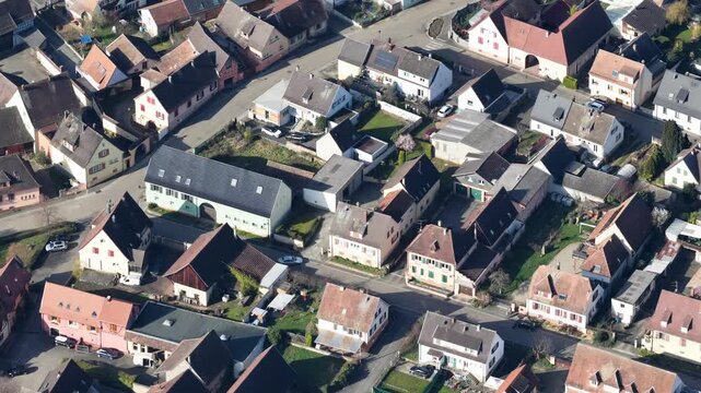 Aerial view of rooftops with red and brown hues, interspersed with roads cutting through the village, creating a tapestry of textures, Mittelwihr, Grand Est, France.