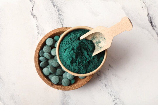 Bowls of spirulina powder and tablets with scoop on marble background