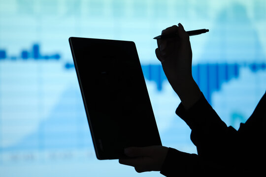 Silhouette of young businesswoman's hands with tablet computer on charts background, closeup. Data science concept