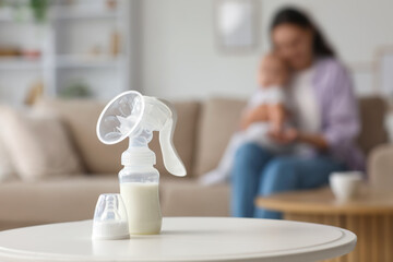 Breast pump on table against mother with baby at home, closeup