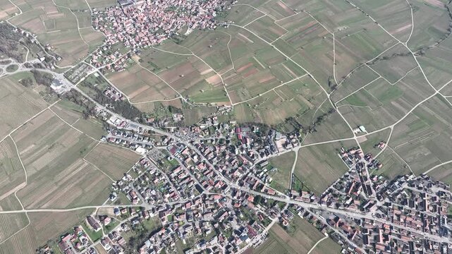 Aerial view of Mittelwihr village, amidst patchwork fields, roads, and buildings, creating a textured landscape, Mittelwihr, Grand Est, France.