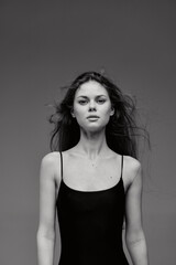 Black and white portrait of a young woman with loose hair wearing a black sleeveless top against a...