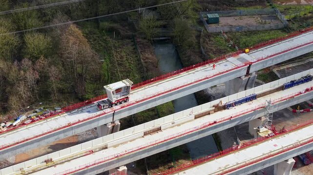 Aerial view of HS2 construction site with concrete flyovers and heavy machinery amidst lush greenery, Birmingham, United Kingdom.
