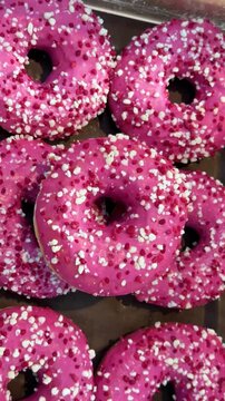 Many bright pink frosted doughnuts with white and red sprinkles confectionery display