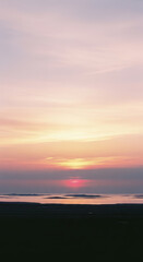 Fototapeta premium The sun sets over a flat body of water creating a band of intense pink and orange color across the lower sky.