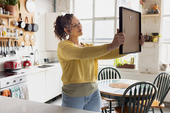 Young woman planning where to hang a picture in her new home