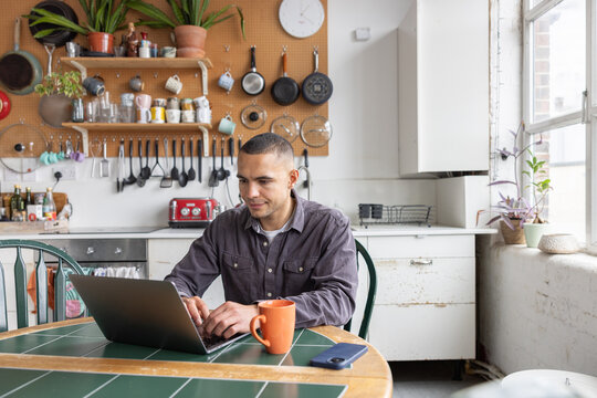 Young man paying bills online in the kitchen