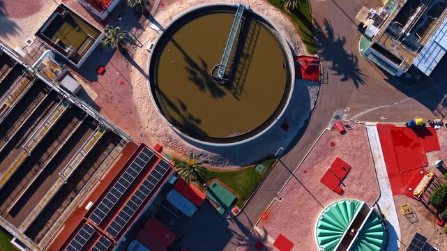Circular wastewater clarifier and solar panels. Detail of a circular sedimentation tank with a bridge and rooftop solar panels at a treatment plant.