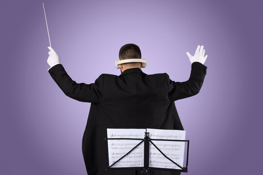 Young male conductor with note sheets and headphones on lilac background, back view