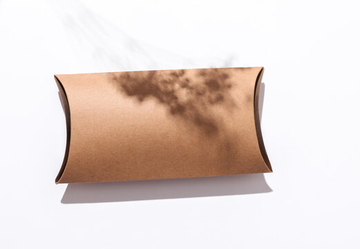 Eco-friendly pillow box with a shadow from sunlight and dry grass on white background