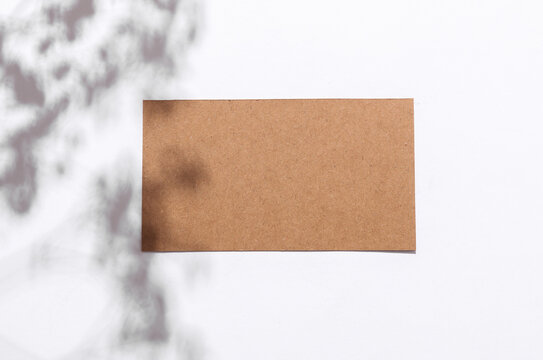 Cardbord brown business card with shadow from sunlight on a white background