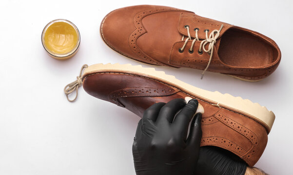 Shoemaker applies shoe polish to leather shoes on a white background