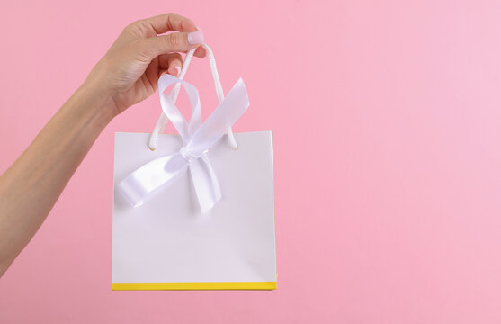 Female hand holding premium white paper bag with bow mockup for jewelry products on pink background