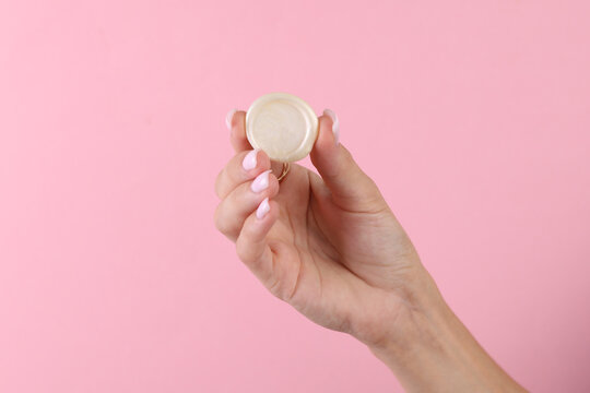 Woman's hand holds a round sealing wax on a pink background