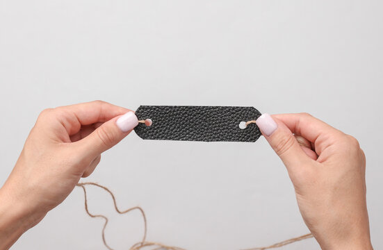 Hands holding leather sample or tag on gray background