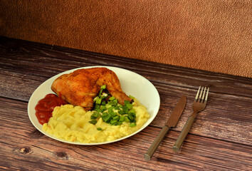 Baked chicken leg with mashed potatoes, tomato sauce and chopped green onions in a round plate on a...