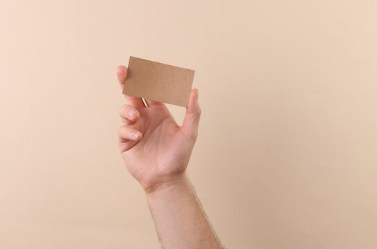 Hand holding Cardboard brown bisiness card on a beige background