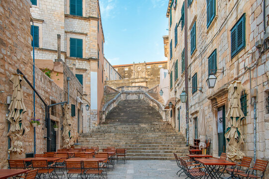 Baroque stone staircase in Dubrovnik old town leading to St. Ignatius Church with limestone buildings on narrow street with traditional architecture and outdoor cafe tables, Dalmatia, Croatia