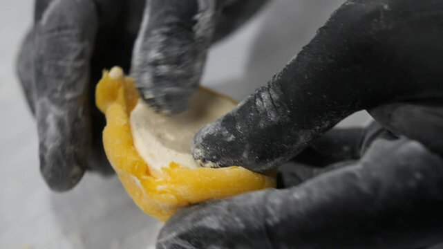 Skilled confectioner hands cover cream filling with mango rice dough in bakery closeup. Japanese baker cooks delicious cake with tropical fruits at kitchen countertop. Cuisine secrets