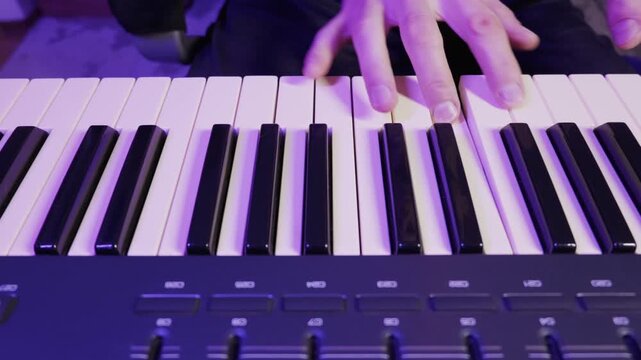 Musician hands play a melody on an electronic MIDI keyboard synthesizer. Vibrant purple and blue neon lighting illuminates the close-up studio shot.