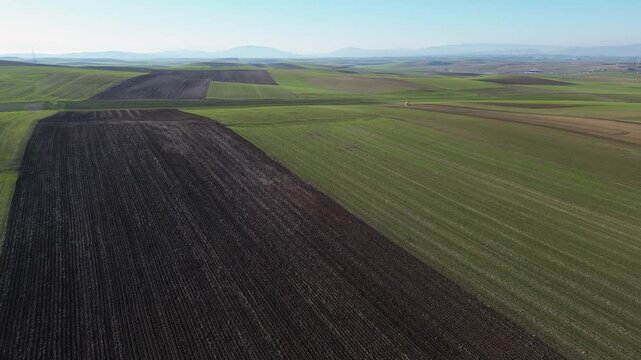 Cinematic drone pull-back shot revealing a vast patchwork of fertile farm fields in Thessaly. Striking visual patterns of ploughed soil and green crops. Ideal for agriculture storytelling.