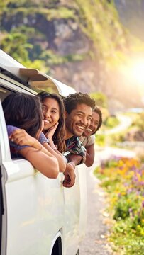 Joyful friends on a road trip, heads out of car window, enjoying scenic mountain views and sunny weather.