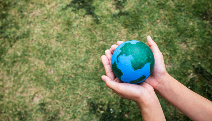 Child hands holding a hand-painted Earth globe over a green grass background. Symbolic of environmental protection, sustainability and save the planet concept.