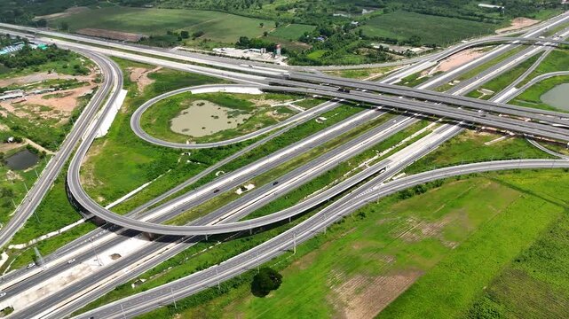 Aerial view of modern highway interchange with multilayer roads and curved ramps surrounded by green farmland, showcasing transportation infrastructure, urban development, and road network planning.