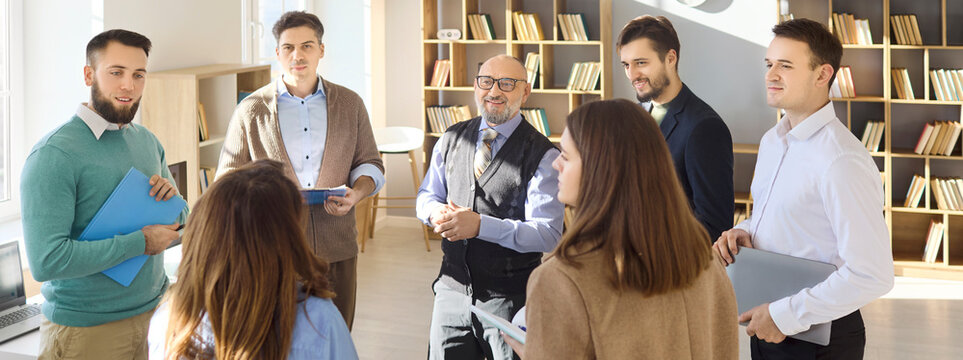 Teacher mentor with students in group meeting. Adults stand in a classroom sharing ideas and discussion. They collaborate on training education tasks and teamwork. Team coach group learning concept.