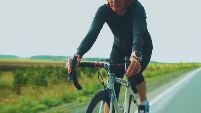 Cyclist riding road bike on countryside road. Woman athlete training outdoors with helmet and sunglasses. Healthy lifestyle, endurance sport and fitness activity in nature.