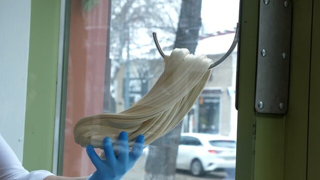 Close-up of a white caramel stretched on a metal hook in a pastry shop, against the background of a large window, preparing traditional caramel candies, and producing caramel candies.