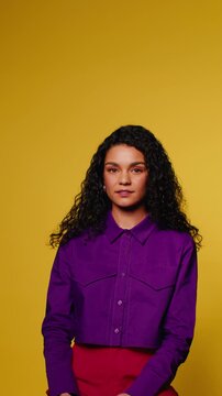 Young woman smiles confidently in purple shirt against yellow background