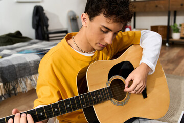Obraz premium Stylish teenager enjoys playing guitar at home in a cozy indoor setting
