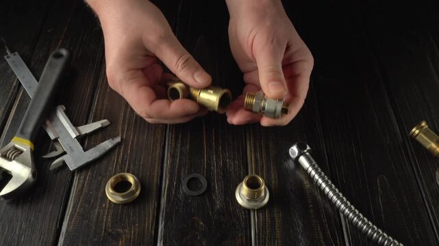 Hands assembling plumbing fittings with brass connectors and tools on a wooden work surface, showcasing detailed mechanical work in progress