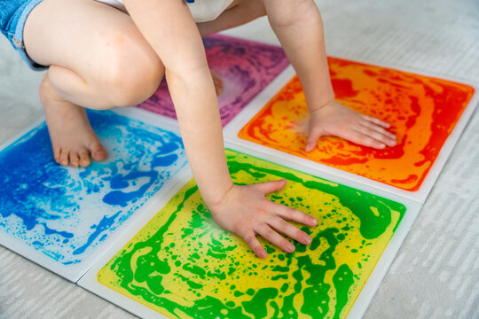 Little girl pressing colorful sensory gel mats with hands and feet while playing on floor. Sensory integration and motor development concept for autism support and occupational therapy activity.
